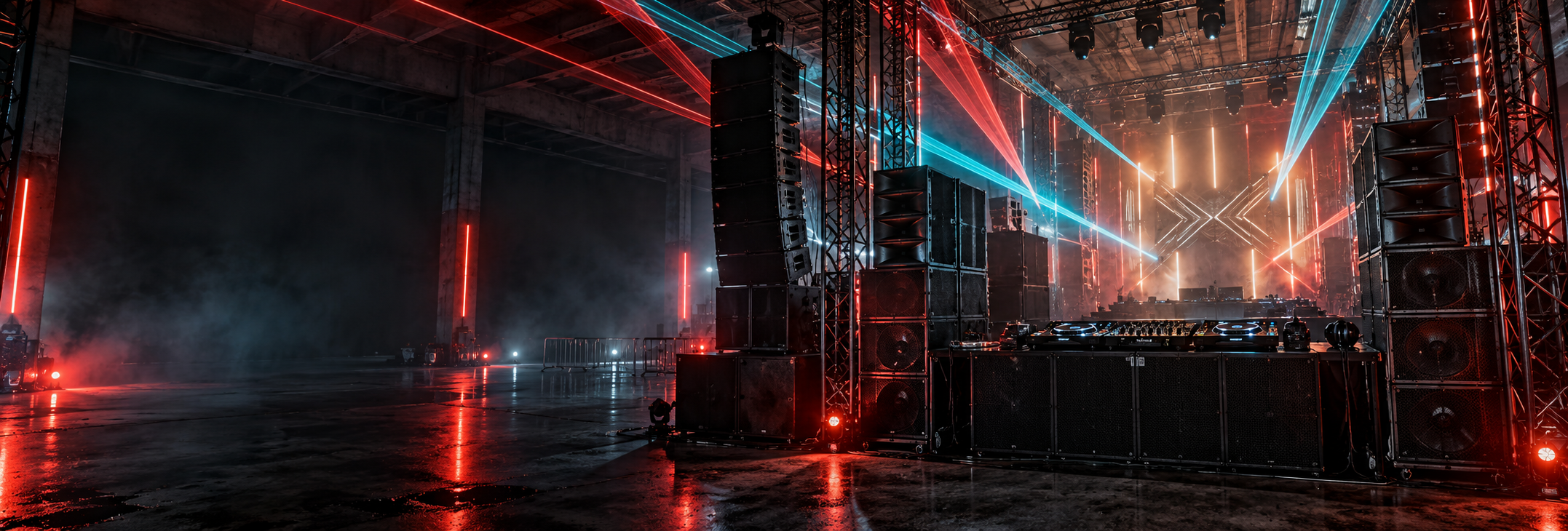 Industriële hard-dance stage met zware speakerstacks, DJ-apparatuur en rood-cyaan licht.
